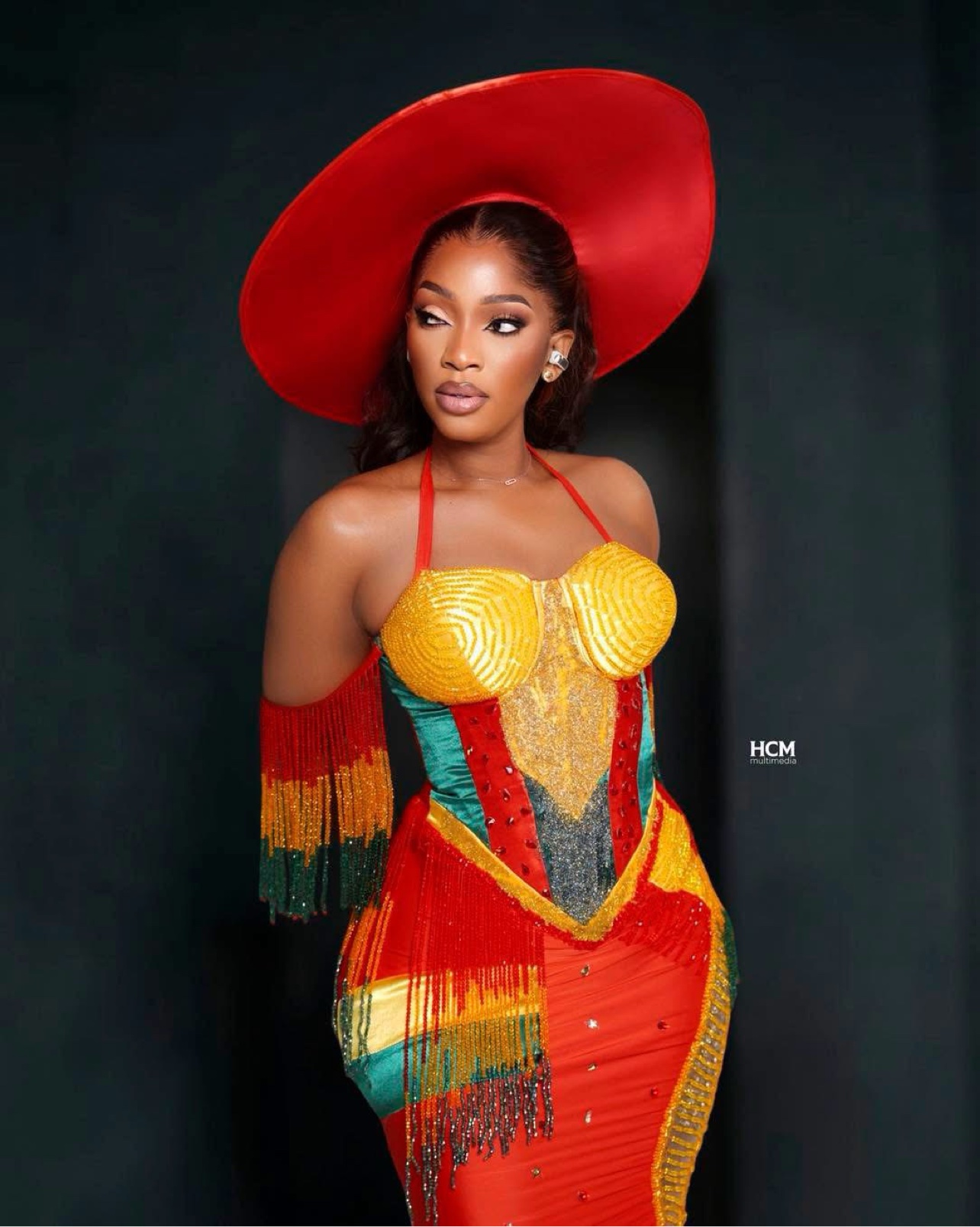 Djelykaba Bintou en portrait éditorial, grand chapeau rouge et robe aux couleurs vives perlée